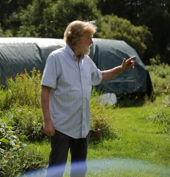 Gregory Wilson beside a high tunnel in Vershire, pointing toward the fields